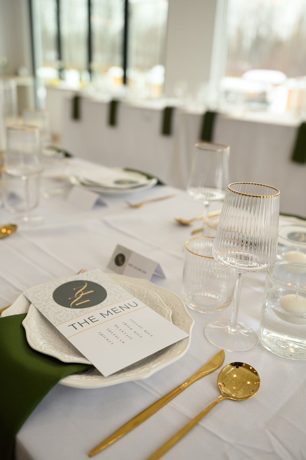 A layered place setting with gold-rimmed fluted glassware, gold cutlery, a green napkin and a printed menu